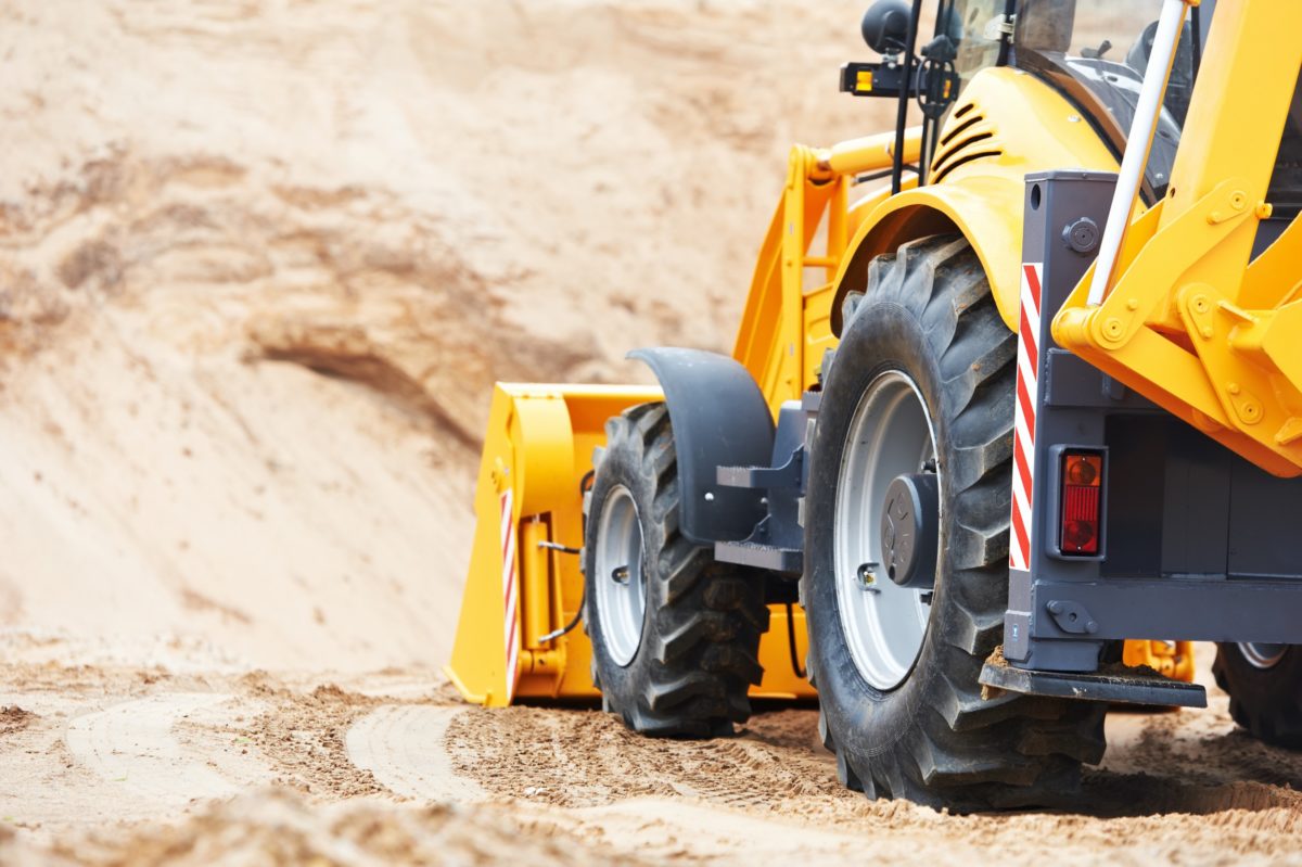 A yellow tractor with a plow attachment on the back of it.