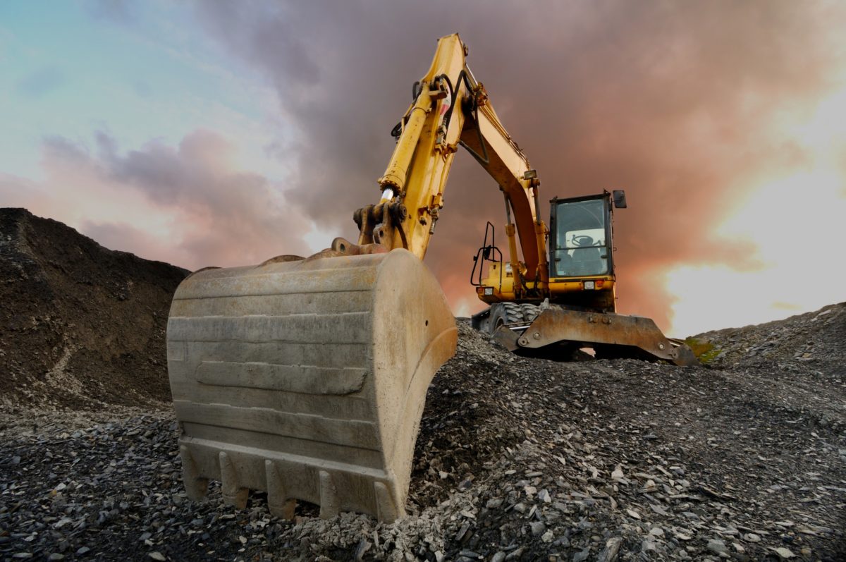 A yellow and black excavator on top of some rocks